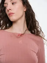 Remera de manga larga entallada confeccionada en tejido pointelle suave, con escote a la base y detalle de pequeño lazo decorativo en el centro. Presenta terminaciones con borde picot.