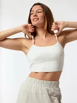 Top deportivo crop top blanco con tirantes delgados, escote recto y costuras decorativas que simulan un corset en la parte frontal.