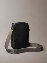 Cartera estilo reportera de Calvin Klein confeccionada en cuero sintético granulado negro. Posee un compartimento principal y un bolsillo frontal con cierre de cremallera, además del monograma de la marca grabado en relieve. Incluye una correa ajustable de color verde oliva.