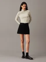 Top color crema de algodón con textura de canalé, corte slim, largo cropped, cuello alto y manga larga.