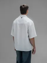 Camisa blanca de manga corta, con cuello clásico y cierre de botones frontal.