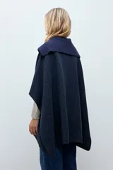 Capa de paño color marrón con cuello solapa y panel central de tejido acanalado. Cuenta con cierre frontal de tres botones grandes y diseño holgado.