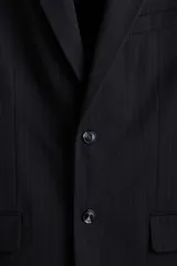 Blazer de botonadura sencilla con solapas de muesca, cierre de dos botones y abertura doble trasera. Presenta un diseño a rayas finas, bolsillo superior, bolsillos delanteros con solapa y botones decorativos en los puños. Cuenta con forro interior y dos bolsillos internos.