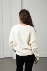 Saco de punto color blanco con cuello en V, cierre frontal con botones y apliques de flores bordadas en relieve. Presenta diseño de ochos y mangas largas con puños acanalados.