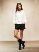 Blusa de color blanco hueso con escote en V y cierre frontal de botones pequeños. Presenta mangas largas con puños ajustados y un diseño de corte recto.