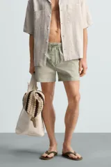 Bañador de hombre color verde claro con finas rayas blancas verticales (efecto seersucker). Tiene cintura elástica ajustable con cordón verde, bolsillos laterales y un bolsillo trasero de vivo.