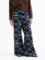 Pantalón de poplin satinado azul marino con estampado de rombos formados por cadenas y bocas en color crema. Presenta un calce wide leg, elástico en la cintura y tiras laterales con vivo.