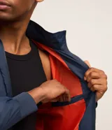 Campera rompevientos azul marino con capucha, cierre frontal y bolsillos laterales. Presenta estampado de NASA en el pecho, parche de bandera estadounidense en la manga y bolsillo utilitario en el brazo.