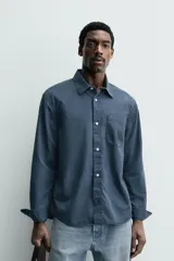 Camisa de corte relajado confeccionada en una mezcla de lyocell y algodón con efecto lavado. Presenta cuello solapa, manga larga con puños abotonados, bolsillo de plastrón en el pecho y cierre frontal con botones.