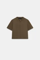 Chaqueta de punto color verde militar, de cuello redondo y manga corta. Presenta un cierre frontal con un único botón dorado.