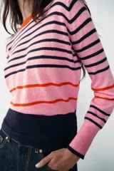 Jersey de punto de cuello redondo y manga larga con puños ajustados. Presenta un diseño de rayas horizontales en tonos rosa, azul marino y detalles en rojo.