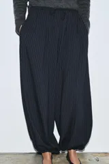 Pantalón de tiro medio, color negro con rayas diplomáticas finas blancas. Cintura elástica ajustable con cordones y bajo abullonado con elástico.
