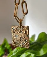 Collar de plata con medalla rectangular texturizada e incrustaciones de cristales verdes, suspendido de una cadena de eslabones.