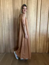 Vestido largo de denim azul, con escote en V, sin mangas, corte holgado, bolsillos laterales y aberturas en los costados de la falda.