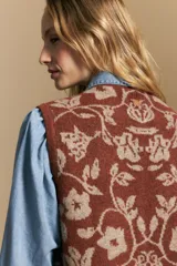 Chaleco tejido de punto con diseño floral ornamental, de silueta recta y cierre frontal con botones. Presenta una estética romántica y sofisticada, ideal para superponer sobre otras prendas.