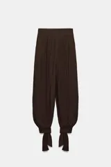 Pantalón bombacho de tiro alto, color marrón, con efecto arrugado y cintura elástica en la espalda. Cuenta con pinzas delanteras, bolsillos frontales, pernera abullonada y puños acabados en lazo.
