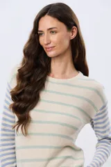 Buzo tejido de algodón con diseño a rayas horizontales, cuello redondo y mangas largas. El cuerpo presenta rayas en tonos azul y beige, mientras que las mangas combinan rayas en tonos azul y rosado.