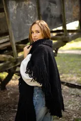 Poncho de lana merino color negro, con cuello alto, diseño amplio y terminaciones con flecos en todo el borde.