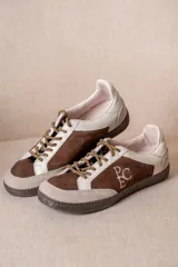 Championes de estilo urbano en combinación de tonos marrones y crema, confeccionados en gamuza y cuero. Presentan cordones jaspeados, suela de goma y detalle de logo bordado en el lateral.