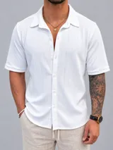 Camisa de manga corta color blanco con textura vertical sutil, cuello camisero y cierre frontal con botones. Confeccionada en algodón premium.