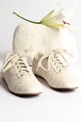 Zapatillas bajas color crema con cordones y suela marrón.