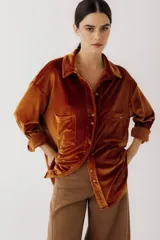 Camisa color marrón anaranjado de terciopelo, con cuello clásico, cierre frontal con botones, dos bolsillos de parche en el pecho y mangas largas con puños abotonados.