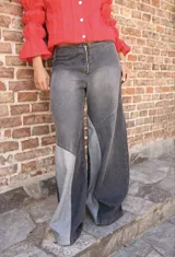 Pantalón de jean de corte wide leg con diseño de paneles en combinación de tonos negro y gris. Presenta cierre frontal con cremallera dorada y costuras decorativas en la zona de la cintura.