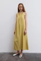 Vestido midi color amarillo con cuello halter, espalda descubierta y lazada en el mismo tejido.