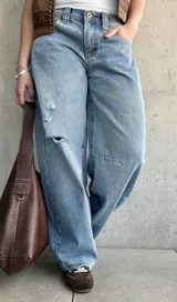 Jean de denim celeste de corte barrel, tiro bajo, con roturas y detalles desgastados en la rodilla.