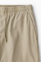 Pantalón de algodón color beige, estilo casual con corte relajado, cintura elástica con cordón de ajuste oculto y bolsillos al bies y traseros.