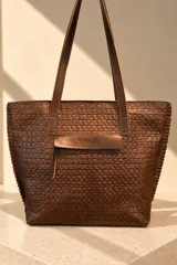 Bolso tipo tote bag color marrón chocolate, confeccionado 100% en cuero vacuno con textura símil cocodrilo. Presenta doble asa larga para hombro, costuras laterales con pasamanería y detalle colgante de borla de flecos de cuero.