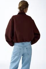 Campera oversized de sarga color marrón, con cuello, cierre frontal y bolsillos laterales ribeteados. Cuenta con mangas abullonadas, puños elásticos y bajo globo para una silueta redondeada.