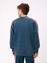 Sweater de cuello redondo marca Rusty, con diseño de bloques de color en azul marino y verde, con detalles de líneas blancas. Presenta el logo de la marca bordado en el pecho.