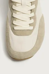 Zapatilla deportiva estilo barefoot, color marrón, con diseño de paneles en combinación de materiales y detalles en serraje. Cuenta con puntera redondeada y ancha, cordones en color crema y suela fina de goma flexible en contraste.