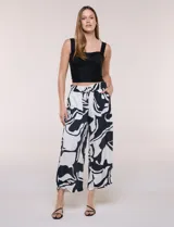 Pantalón ancho negro y blanco con estampado abstracto, cintura elástica con cordón ajustable, bolsillos delanteros con detalles de pompones y corte tobillero.