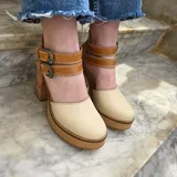 Zapatos de tacón alto con plataforma, confeccionados en cuero color marfil y marrón tostado, con taco ancho de madera y doble tira con hebillas metálicas ornamentadas en el empeine.