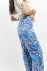 Pantalón cargo de tiro alto, color azul vibrante con estampado de círculos y estrellas en tonos morados y blancos. Presenta un calce ancho y holgado, con elástico ajustable en la parte trasera de la cintura y frunce en los tobillos que puede ajustarse o dejarse suelto.