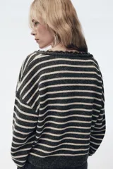 Jersey de punto a rayas horizontales en color gris y beige, con escote en pico profundo y detalle de encaje negro en el borde. Presenta mangas largas y corte ligeramente cropped.