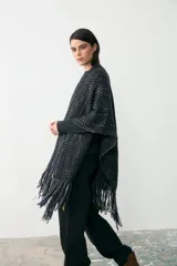 Ruana tejida artesanalmente en lana, con diseño de textura tramada en tonos oscuros con detalles en colores tierra. Presenta un cuello alto y mangas integradas de punto liso.