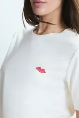 Pijama compuesto por una remera de cuello redondo en color blanco con un pequeño estampado de labios rojos en el pecho y un pantalón largo de corte holgado con estampado de rayas verticales y labios rojos sobre fondo claro.