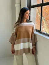 Poncho de punto con diseño de rayas horizontales en tonos tierra, blanco y beige. Presenta un corte holgado, cuello redondo y mangas anchas con puños acanalados.