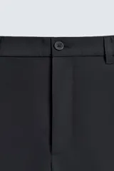 Pantalón de corte regular fit, color negro, confeccionado en tejido elástico. Presenta cintura elástica, cierre frontal con cremallera y botón, bolsillos laterales y bolsillos traseros de vivo.