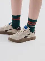 Zapatillas urbanas de cuero en tono off-white, con detalles en color marrón oscuro y suela de goma texturizada en contraste. Presentan cordones al tono y logo de la marca grabado en el lateral.