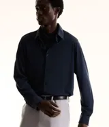 Camisa de manga larga para hombre, color azul marino, con cuello inglés y abotonado frontal. Confeccionada en tejido piqué de poliamida y elastano con tecnología performance que ofrece elasticidad, secado rápido y resistencia a las arrugas.