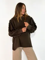 Sweater de punto color bordó, con cuello redondo, mangas largas abullonadas y detalle de flecos en las costuras de los hombros.