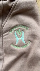 Short de algodón color tostado con bordado frontal que incluye el logo y texto 'Human School Learning Community' en tonos verde y celeste.