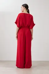 Pantalón palazzo rojo de tiro alto con pliegues marcados en la parte delantera y corte ancho y fluido. La modelo viste un conjunto monocromático con una blusa de manga corta a juego.