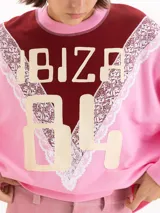 Buzo de cuello redondo en color rosado, con un diseño combinado en el pecho que incluye un panel superior bordó, detalles de encaje y la inscripción "IBIZA 84" en tono beige.