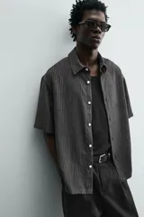 Camisa de corte relajado con textura de rayas verticales, cuello solapa y manga corta. Presenta cierre frontal con botones a tono.