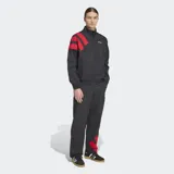 Campera deportiva Adidas de corte holgado, con cierre frontal de cremallera y cuello alto. Presenta un diseño en bloques de color negro con detalles en rojo en las mangas, confeccionada en tejido técnico reciclado.
